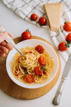 Portion of spaghetti pasta with parmesan and cherry tomatoes sprinkled with spices in a plate on wooden board