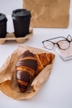 Delicious chocolate croissants and coffee cups at workplace with glasses and notebook, food delivery concept