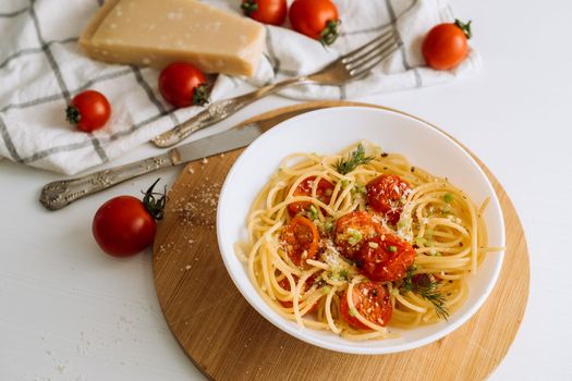 Close up portion of spaghetti pasta with parmesan and cherry tomatoes sprinkled with spices in a plate on wooden board