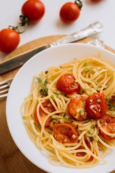 Close up portion of spaghetti pasta with cherry tomatoes sprinkled with spices in a plate on wooden board