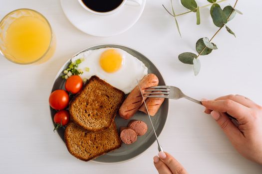 English breakfast with black coffee and orange juice, grilled sausage and whole wheat toast with fried egg and cherry tomatoes on plate