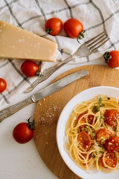 Flat lay portion of spaghetti pasta with cherry tomatoes sprinkled with spices, parmesan cheese and retro knife with fork