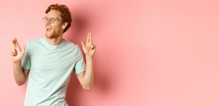 Cheerful redhead guy listening music and dancing, triumphing or celebrating success, standing over pink background.