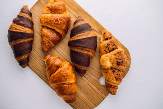 Flat lay of bunch of appetizing brown and chocolate croissants on wooden board on white table