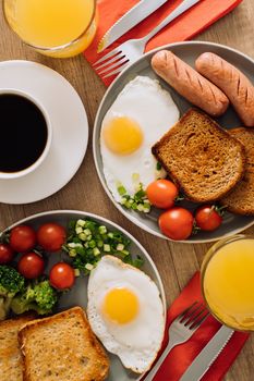 Flat lay of English breakfast with cup of black coffee and orange juice, grilled sausage and whole wheat toast with fried egg and cherry tomatoes