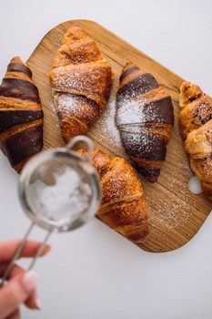 Flat lay appetizing brown and chocolate croissants are sprinkled with powdered sugar