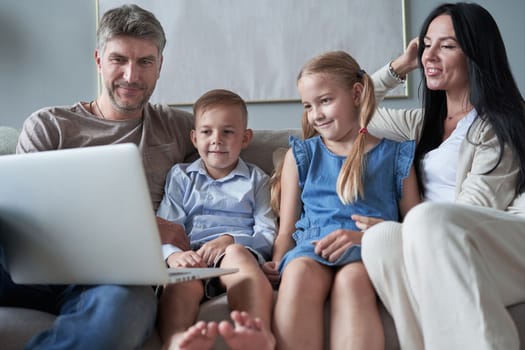 parents and their little kids using laptop at home together