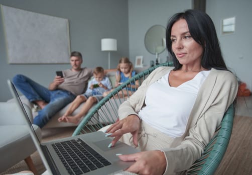 woman using laptop with interest at home while child relax on sofa