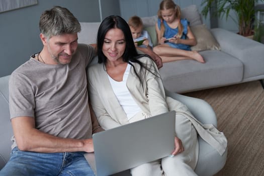 Close up happy parents using laptop sitting on couch at home. Smiling mother and father looking at laptop screen