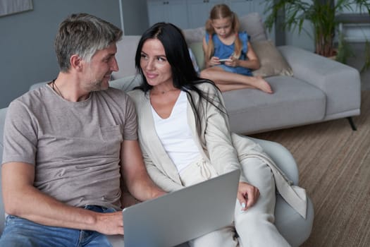 Close up happy parents using laptop sitting on couch at home. Smiling mother and father looking at laptop screen