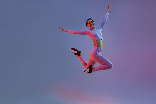 Athletic active woman jumping on studio background with colored filter. Dynamic movement