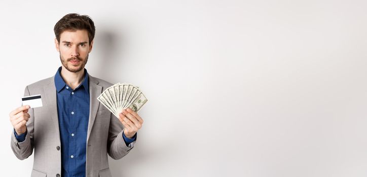 Successful businessman making money, standing in suit with dollar bills and plastic credit card, white background.