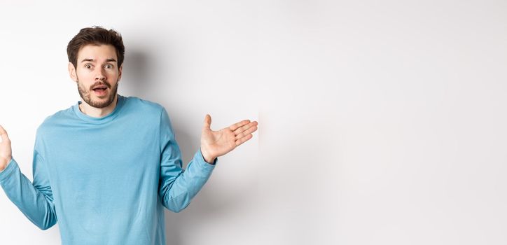 Unbelievable. Amazed young man looking with disbelief, spread hands sideways and staring impressed, standing over white background.