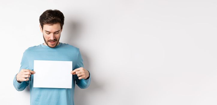 Excited bearded guy reading banner on blank piece of paper, showing logo, standing over white background.