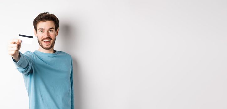 Happy man showing plastic credit card and smiling, recommending bank, standing over white background.