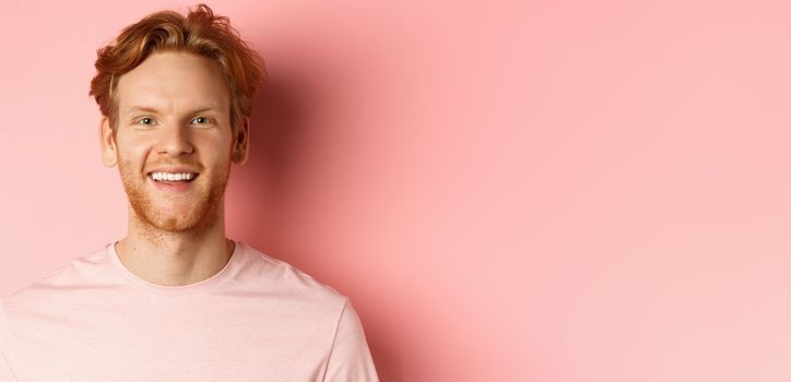 Headshot of happy redhead man with beard and white teeth, smiling excited at camera, standing over pink background.