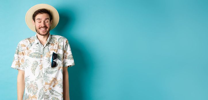 Happy tourist enjoying summer holiday, wearing straw hat and hawaiian shirt, standing joyful on blue background.