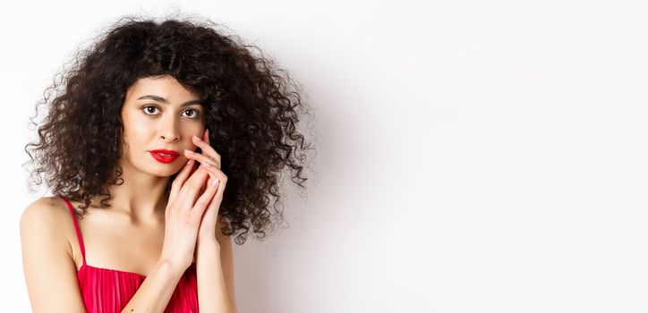 Close-up of tender romantic woman, gently touching face and looking sensual at camera, white background.