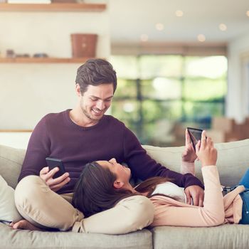 Time together is time well spend. a smiling young couple using digital tablets while relaxing together on the sofa at home