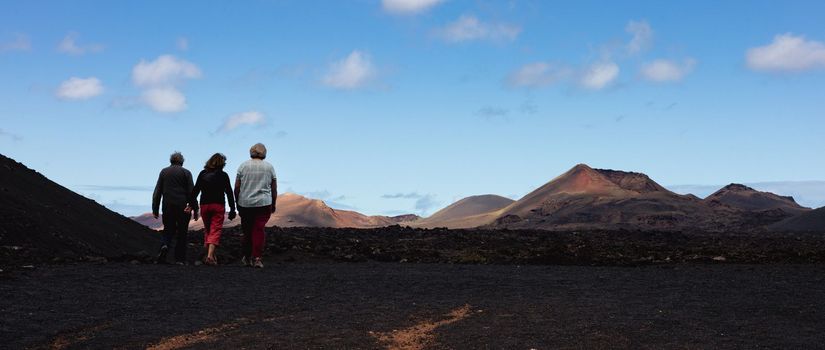 Tourists visiting volcanic landscape of Timanfaya National Park in Lanzarote. Popular touristic attraction in Lanzarote island, Canary Islands, Spain