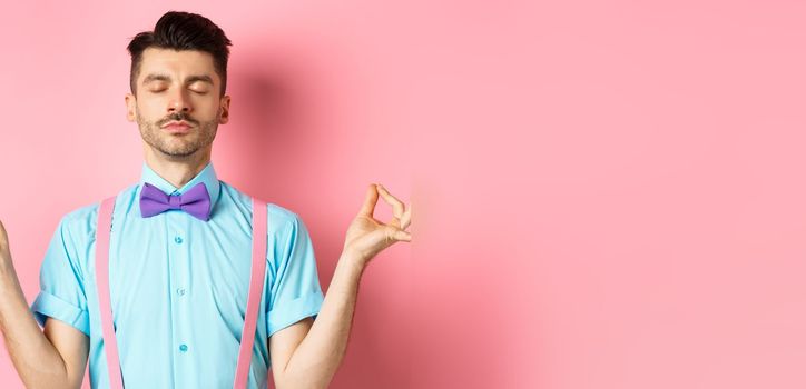 Young guy in bow-tie standing calm and peaceful, meditating with hands in mudra zen gesture and closed eyes, practice yoga to relax, standing over pink background.