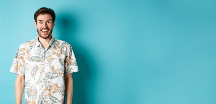 Summer holiday. Handsome happy man in hawaiian shirt looking amused, smiling at camera, standing on blue background.