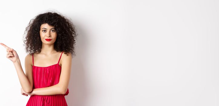 Attractive lady in red dress and makeup pointing finger left, showing logo, standing over white background.