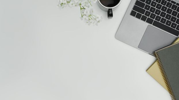 White office desk with laptop computer, books and flowers. Top view with copy space for text.