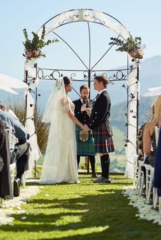 They were made for each other. a cheerful young bride and groom holding each others hands at the wedding alter outside during the day