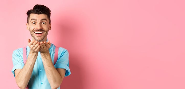 Man in love blowing kiss at camera and smiling passionate, looking at lover happy, enjoying Valentines day, standing over pink background.