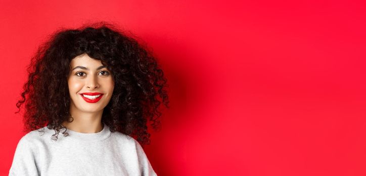 Close-up of beautiful lady with red lips and curly hair, smiling and looking happy at camera, studio background.