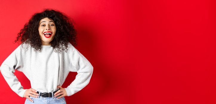 Excited positive woman laughing and smiling, feeling upbeat, looking at funny promo, standing on red background.