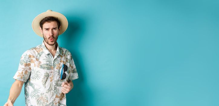 Happy tourist in hawaiian shirt and summer hat dancing, having fun on vacation, standing on blue background.