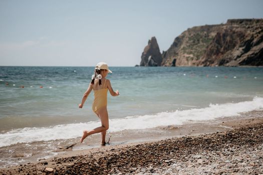 Cute little girl running along the seashore against a clear blue sea and rejoices in the rays of the summer sun. Beautiful girl in yellow swimsuit running and having fun on tropical beach