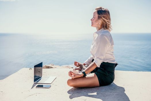 Happy girl doing yoga with laptop working at the beach. beautiful and calm business woman sitting with a laptop in a summer cafe in the lotus position meditating and relaxing. freelance girl remote work beach paradise