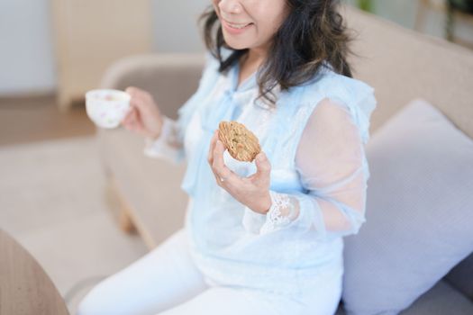 Portrait of an elderly Asian woman drinking healthy tea while eating snack