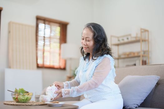 Portrait of an elderly Asian woman drinking healthy tea while eating vegetable salad and snack