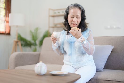 Portrait of an elderly Asian woman drinking healthy tea while eating snack