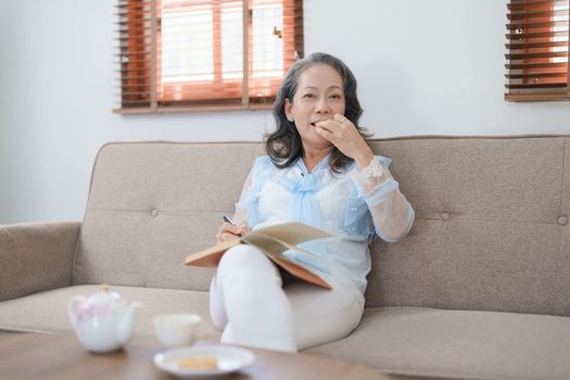 Portrait of an elderly Asian woman holding a notebook eating snacks and drinking tea