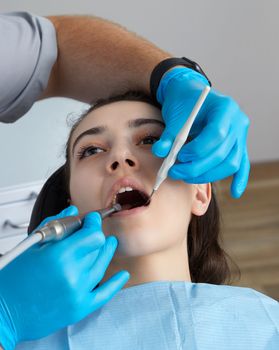 Lady patient sitting in stomatology chair, dentist drilling tooth, modern clinic