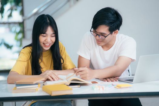 Young asian university students are studying for an exam. There are tutor books with friends. They are classmates that try to help each other. They have been tutoring for many hours in the campus.