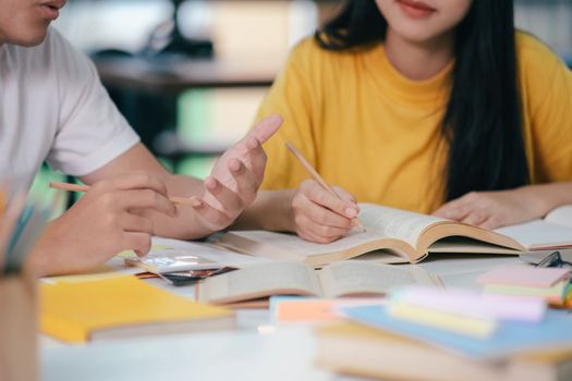 Young asian university students are studying for an exam. There are tutor books with friends. They are classmates that try to help each other. They have been tutoring for many hours in the campus.