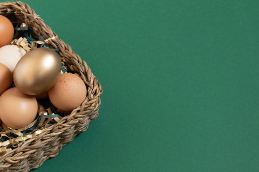 Easter eggs natural and gold in basket with paper filler . Branch of willow catkins. Light pastel orange background with copy space.