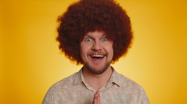 Oh my God, Wow. Excited amazed winner man with Afro hairstyle raising hands in surprise looking at camera with big eyes, shocked by sudden victory. Sincere young hipster guy boy on yellow background