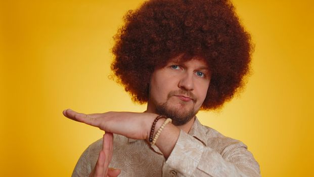 Tired serious upset bearded man with lush afro hairstyle coiffure showing time out gesture, limit or stop sign, no pressure, i need more time, break, pause. Hipster guy on yellow studio background