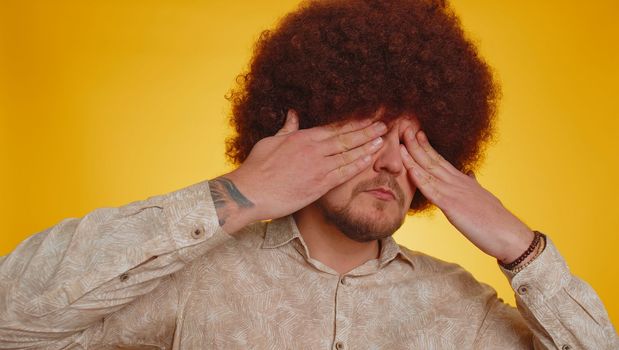 Dont want to look at this, awful. Bearded man with lush afro hairstyle coiffure closing eyes with hand showing stop gesture confused shy scared to watch. Hipster guy boy on yellow studio background