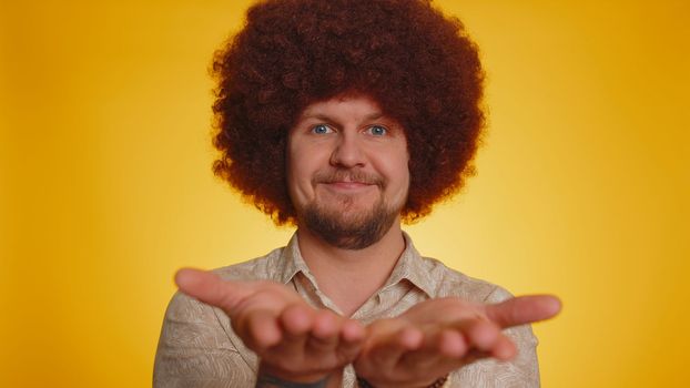 Free gifts and presents for you. Man with afro hairstyle coiffure opening hands, glad to see, excitement, preparing surprise, sharing love emotions, congratulating. Hipster guy on yellow background