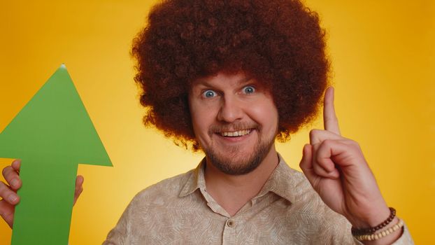 Man winner holding arrow sign pointing up, career growth and money exchange increase. Hipster guy with afro hairstyle showing up indicating successful development progress on yellow studio background