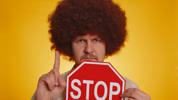 No stop. Serious man say No, hold inscription text red No stop danger sign, warning of finish, prohibited access declining communication, body language, trouble, protest. Guy on yellow background