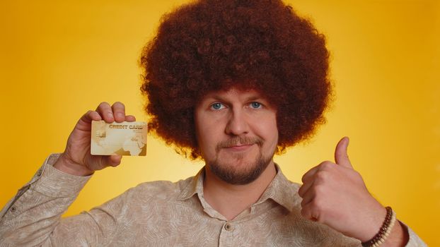 Man with afro hairstyle showing plastic credit bank card advertising transferring money cashless, purchases online shopping, sale discount, internet order delivery purchase. Guy on yellow background